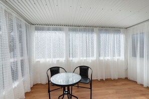 Una habitación con piso de madera, dos sillas negras, una mesa redonda y un techo blanco con diseño acanalado.