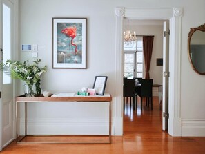 A hallway with a reception desk, a framed painting of a flamingo, a chandelier, and a mirror.