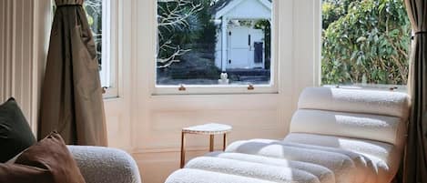 A room with a large window, a sofa, and a chair with a white cushion.