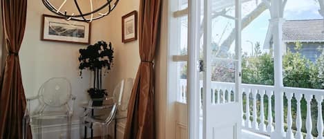 A room with a white door leading to an outdoor balcony, clear chairs, a potted plant, and a hanging light fixture.