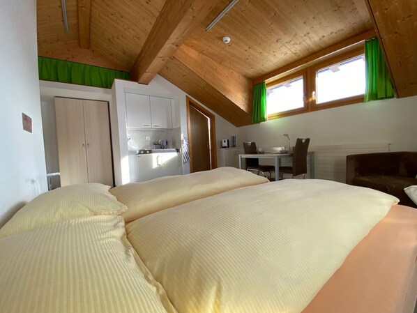 A room with two beds, a kitchenette, and a window with curtains.