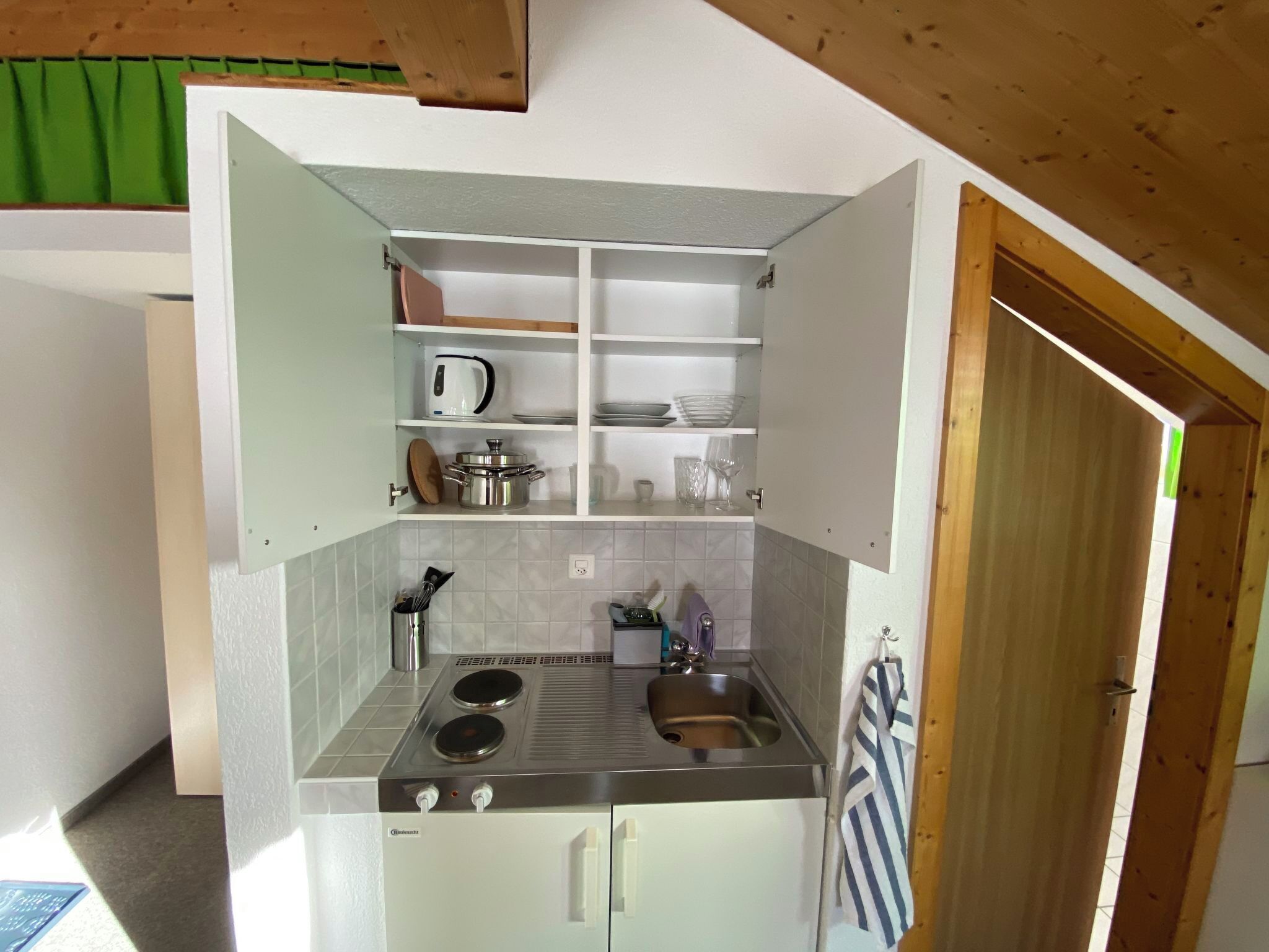 A compact kitchen with a stove, sink, and shelves for storage.