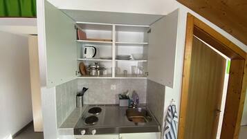 A compact kitchen with a stove, sink, and shelves for storage.