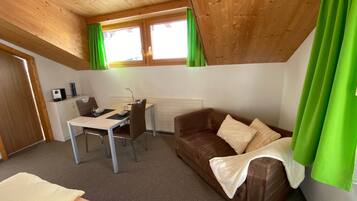A room with a bed, a desk, a brown sofa, and a window with green curtains.