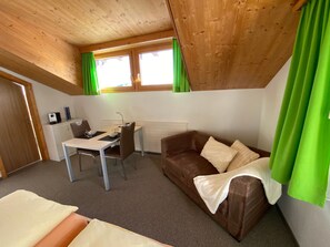 Ein Zimmer mit einem Bett, einem Schreibtisch, einem braunen Sofa und einem Fenster mit grünen Vorhängen.