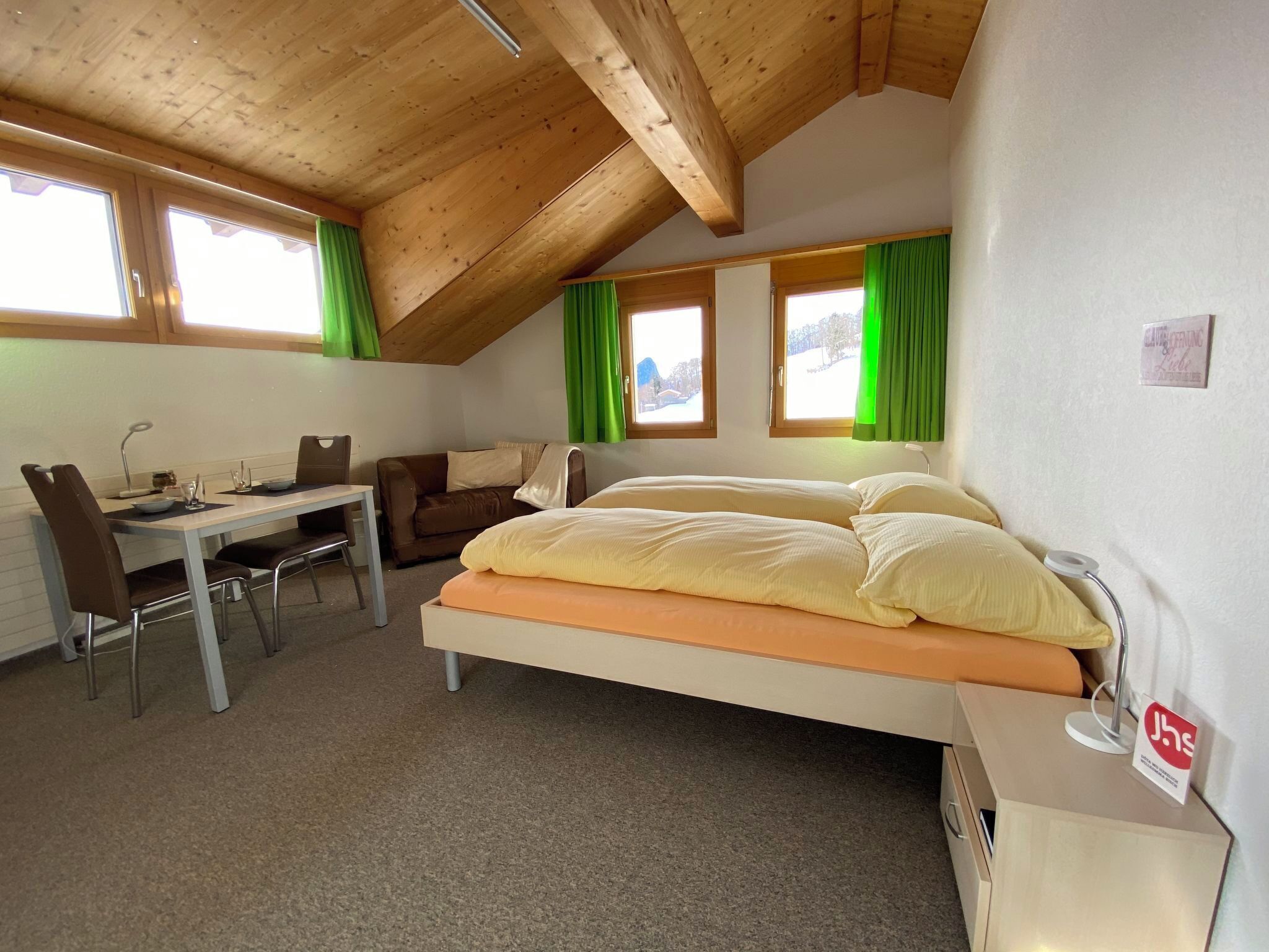 A room with a bed, a desk, a chair, and two windows with curtains.