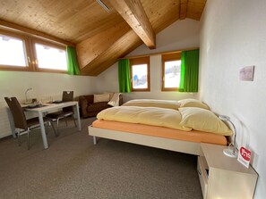 Une petite pièce agréable, dotée d’un lit, d’un bureau et d’une chaise. Elle comporte deux fenêtres avec des rideaux et son plafond est légèrement incliné.