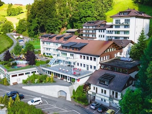 A multi-story hotel with a central courtyard, parking area, and surrounding greenery.