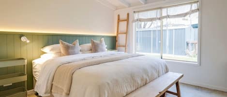 A bedroom with a bed, bedside table, bench, and a window with a view.
