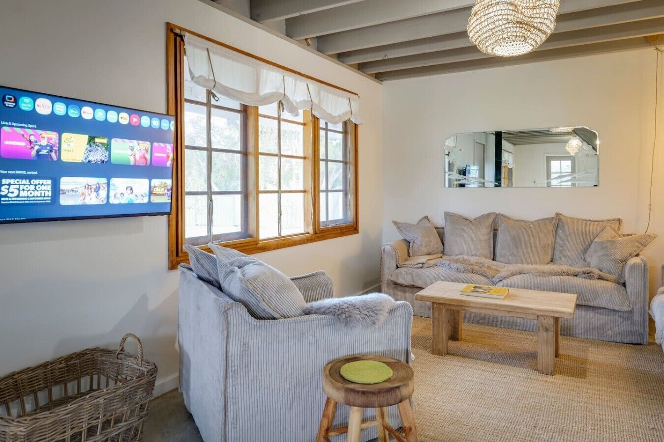A living room with a sofa, a coffee table, a wicker basket, and a television displaying sports content.