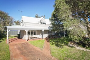 A two-story house with a covered porch, a fenced yard, and a large tree. - Paper Bark Cabin – Dunsborough (Dunsborough)