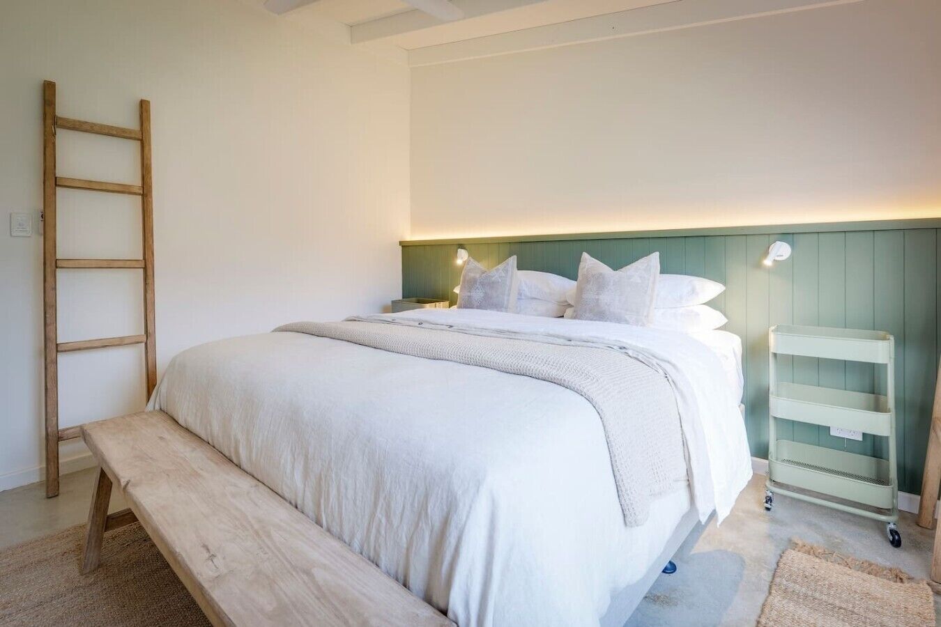 Um quarto com uma cama, uma escada de madeira, uma mesa de cabeceira e uma prateleira na parede.