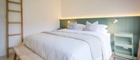 Un dormitorio con cama, una escalera de madera, una mesita de noche y un estante en la pared.