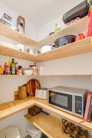 Een kleine keuken met houten planken, een magnetron, een broodrooster en diverse keukengerei.