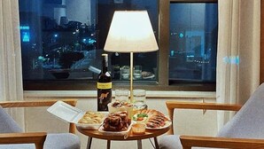 A dining area with a table set for two, a bottle of wine, and a lamp. - Win Sky Hotel (Seogwipo)