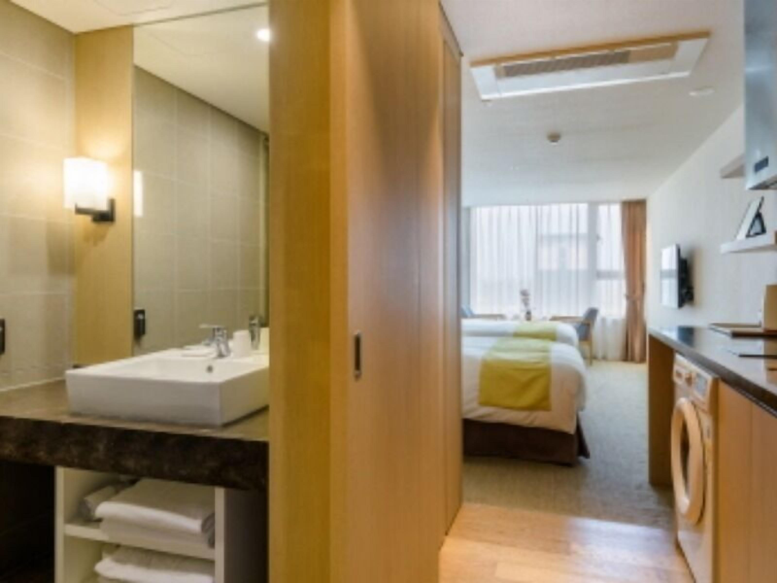 A hotel room with a bathroom, a bed, a desk, and a washing machine.