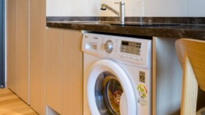 A front-loading washing machine in a kitchen with a wooden floor and a black countertop. - Win Sky Hotel (Seogwipo)