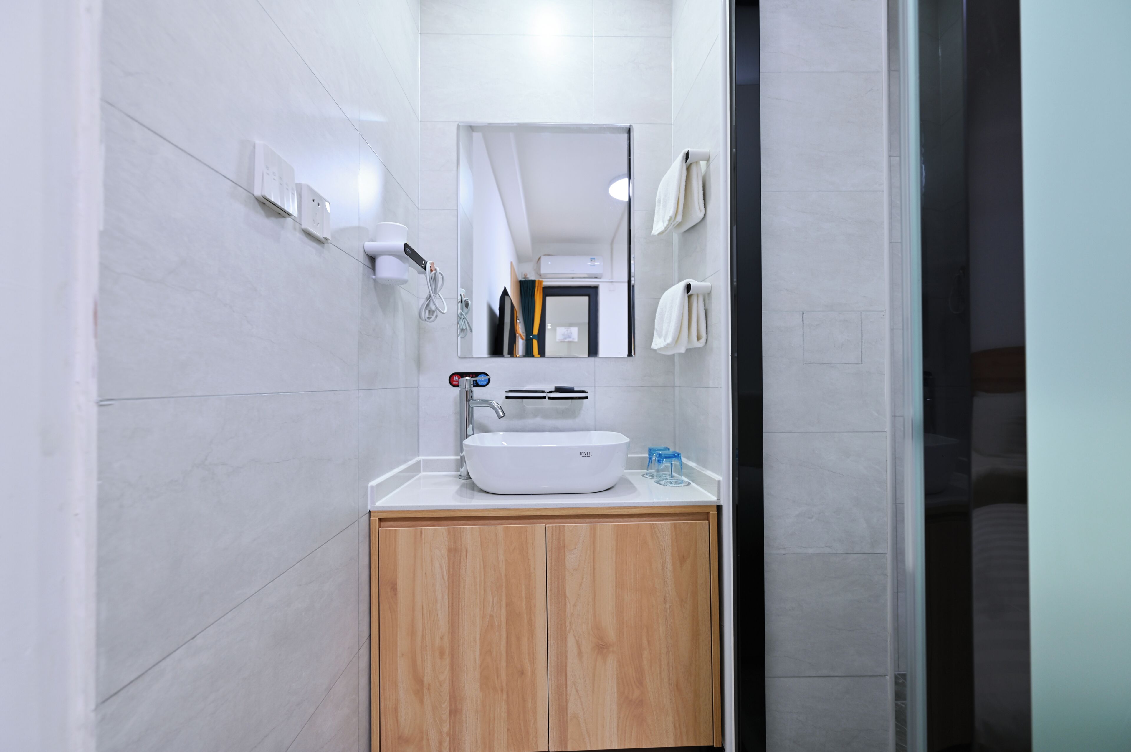 Een moderne badkamer met een witte wastafel, een houten kastje en een spiegel erboven.