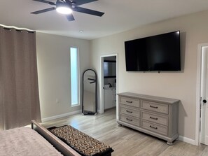 Une chambre à coucher comprenant un lit, une commode, un téléviseur, un ventilateur de plafond et une fenêtre.