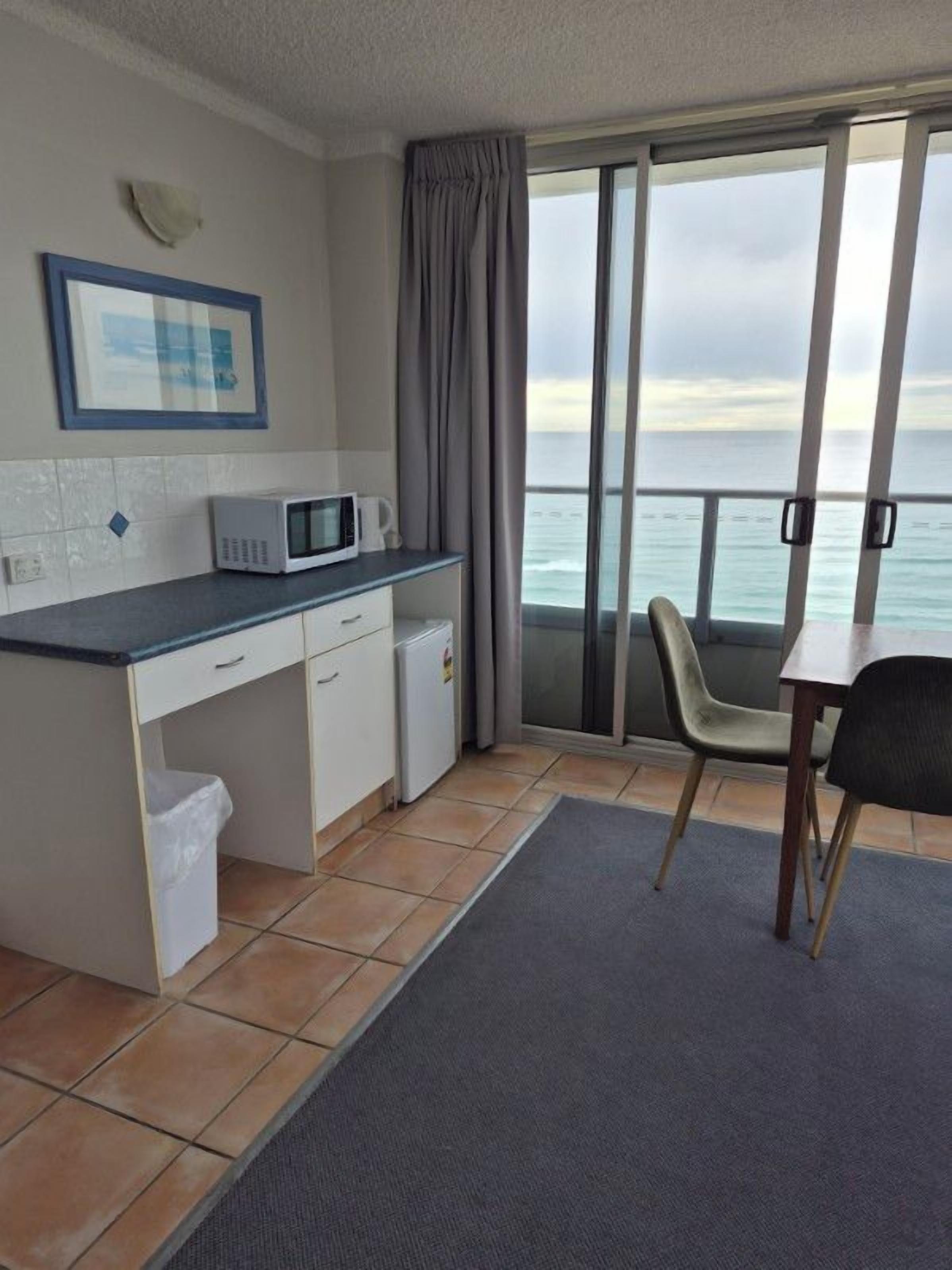 A compact kitchen with a microwave, a small refrigerator, and a window overlooking the sea.