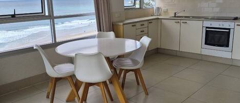 Une cuisine moderne avec des meubles blancs, une table à manger avec des chaises et une vue sur l’océan.