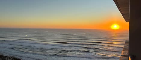 A sunset view from a balcony overlooking the ocean with waves and a clear sky.