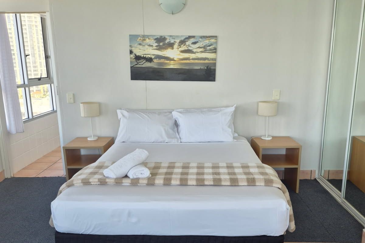 Quarto de hotel com uma cama, duas mesas de cabeceira, um quadro e um espelho grande.