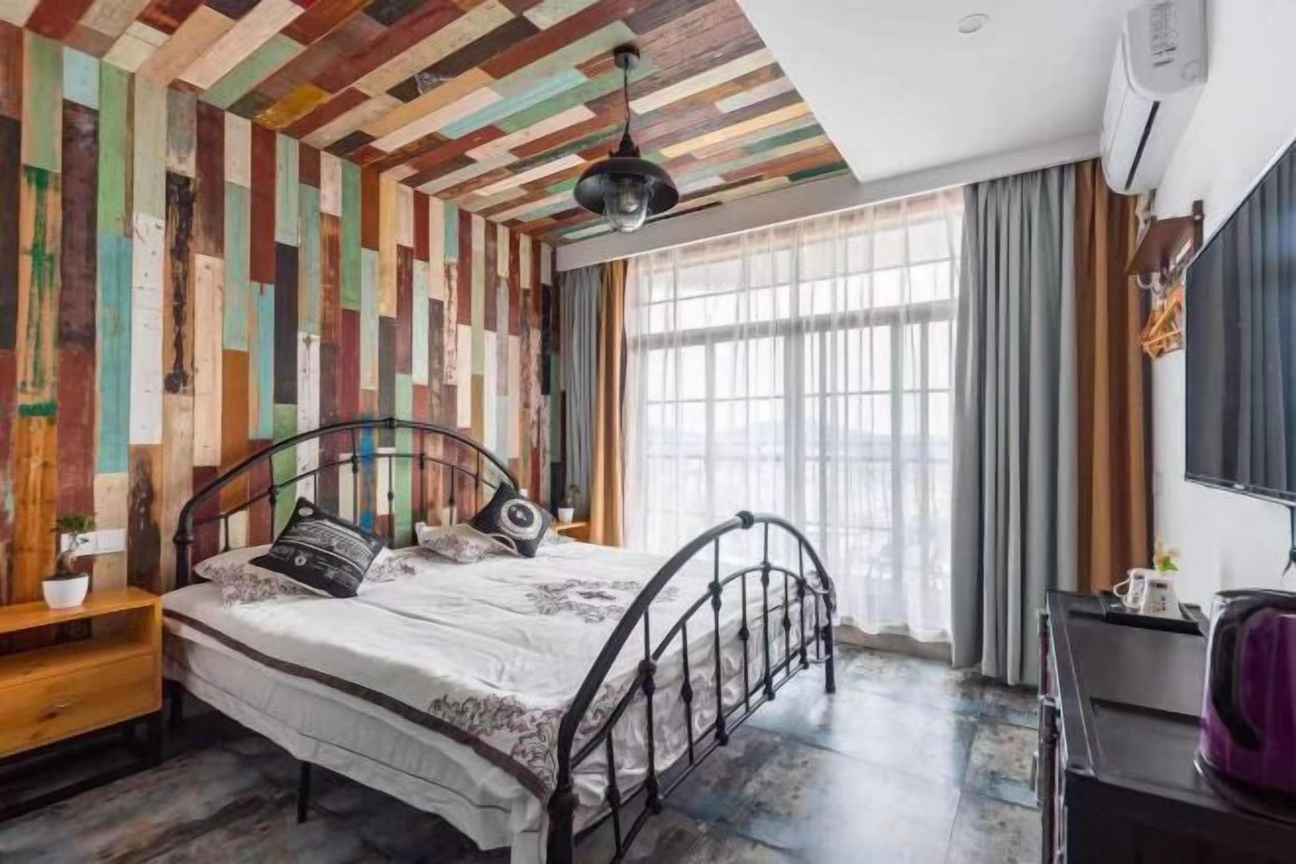 A bedroom with a bed, a desk, a chair, a window, and a wooden wall panel.