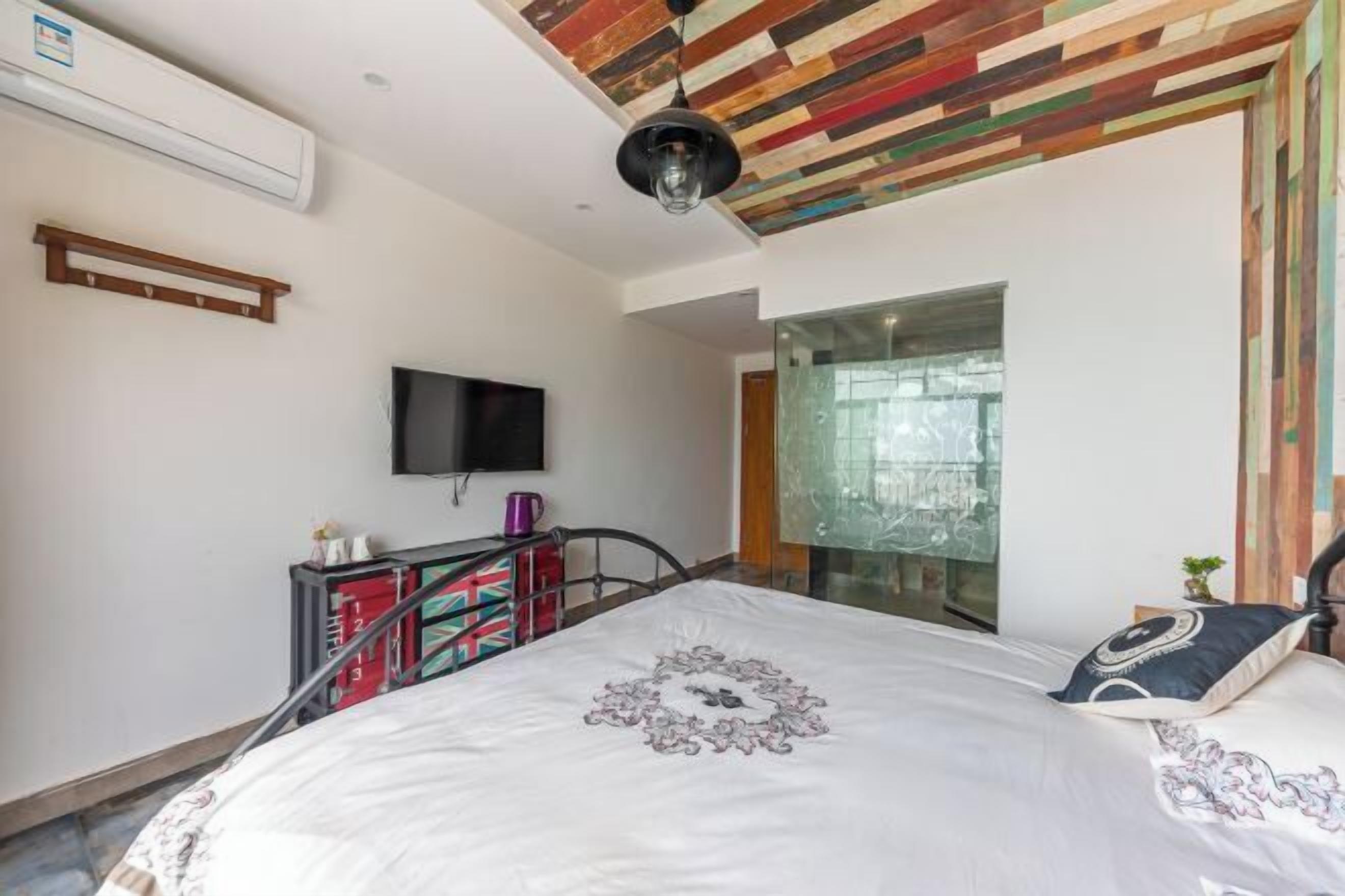 A bedroom with a bed, a television, a window, and a ceiling with a wooden pattern.