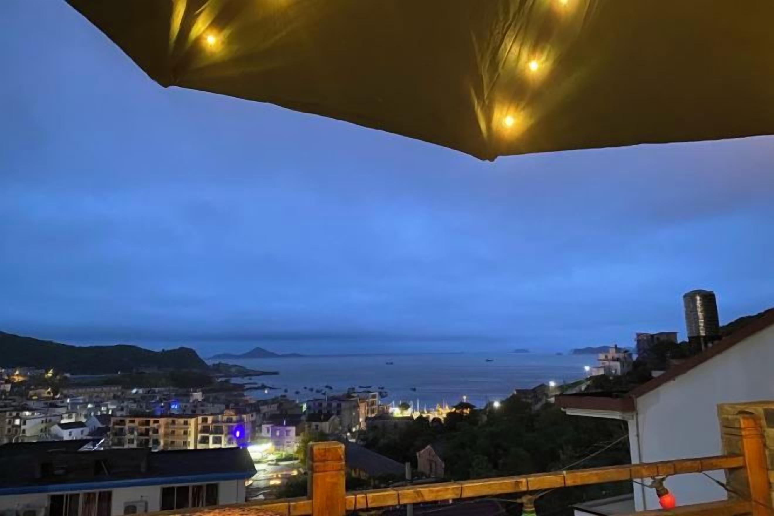 A balcony with a view of a cityscape and the sea at dusk.