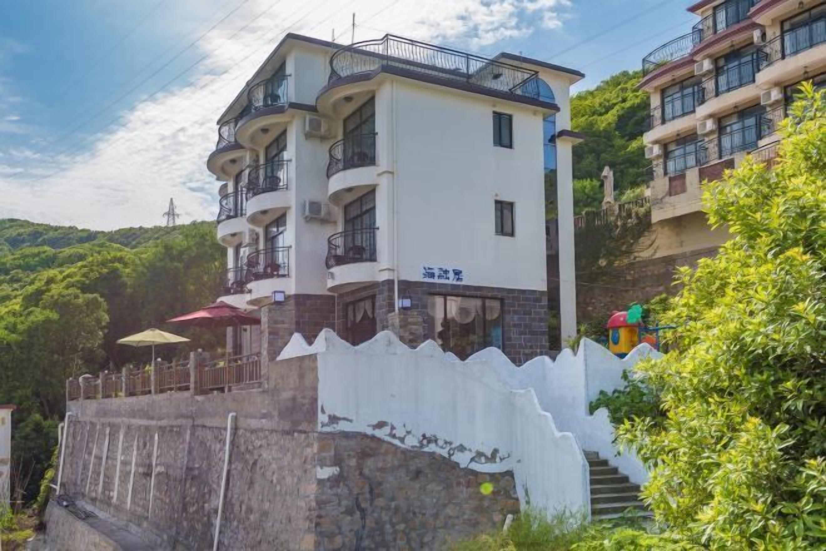 A multi-story hotel with balconies, a white exterior, and a stone wall in front.