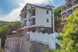 Un hotel de varios pisos con balcones, fachada blanca y un muro de piedra al frente.