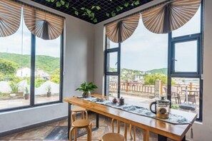 A dining area with a wooden table, chairs, and a view of the landscape through large windows. - Shengsi hairongju seascape homestay (Shengsi)