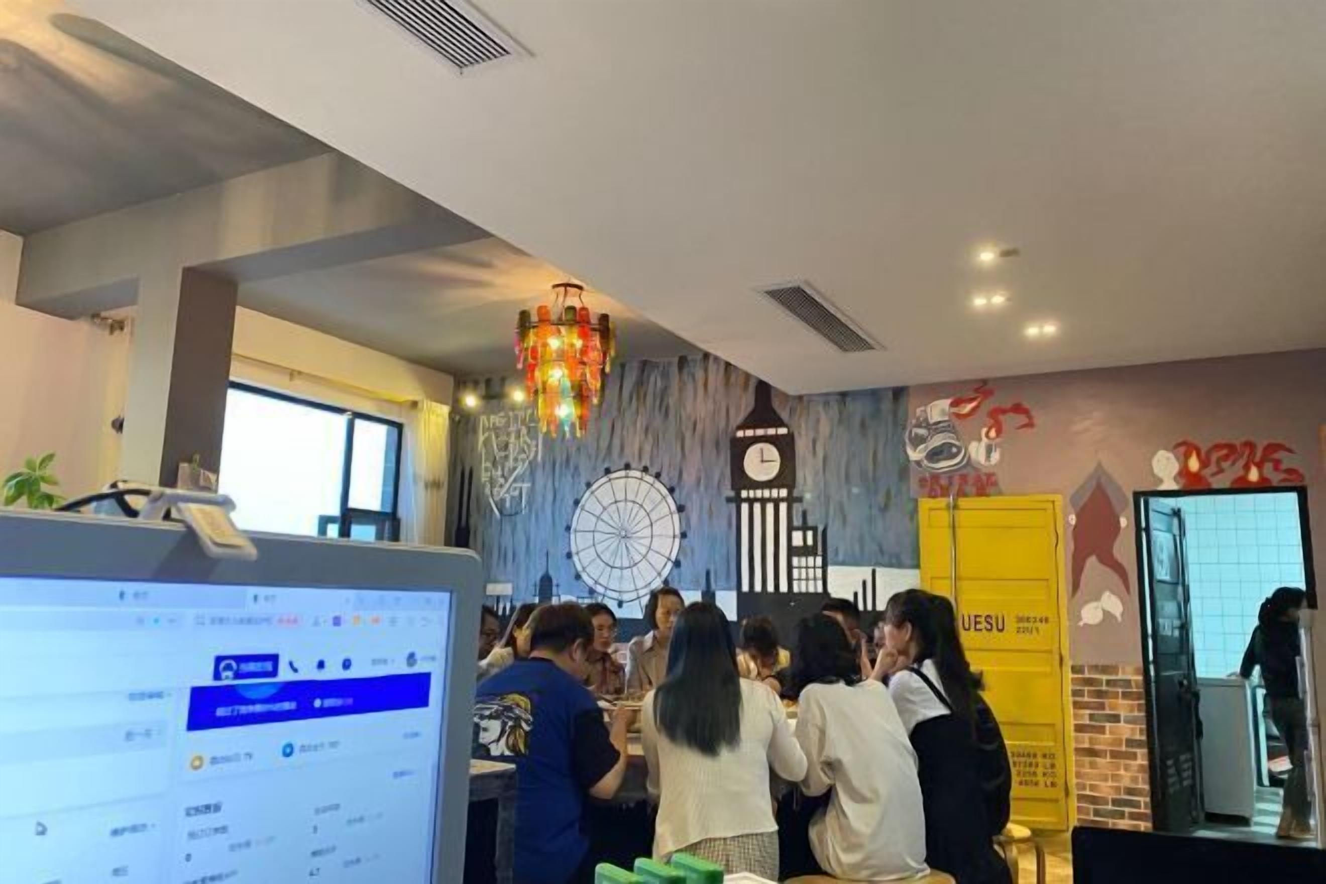 A group of people in a room with a chandelier, a clock, and a wall clock.
