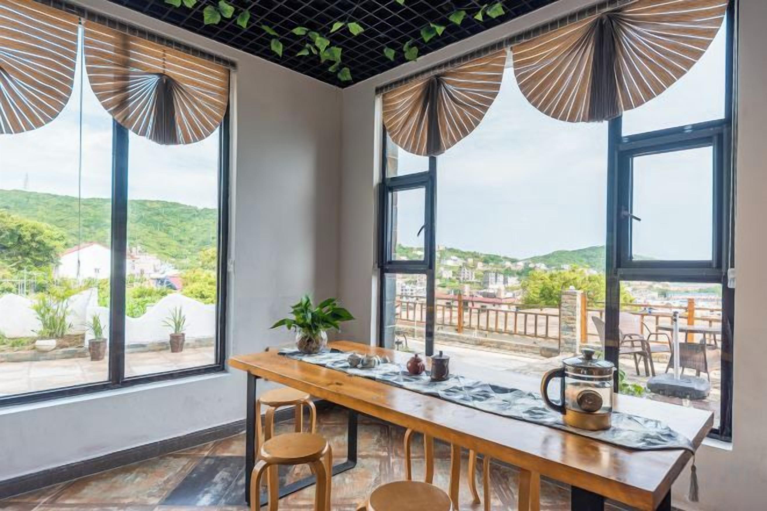 A dining area with a wooden table, chairs, and a view of a hilly landscape through large windows.