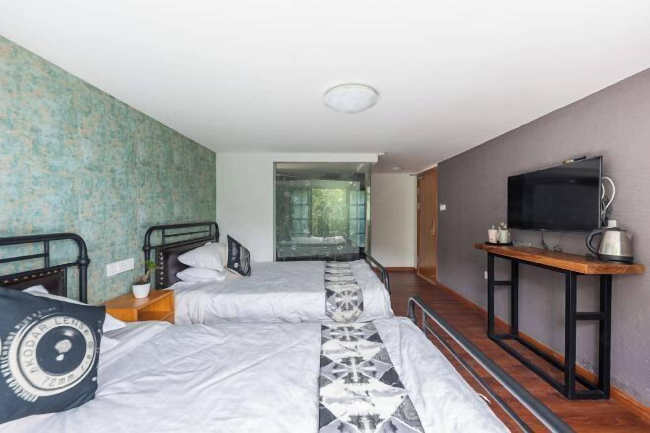 A hotel room with two beds, a television, and a view of a forest.
