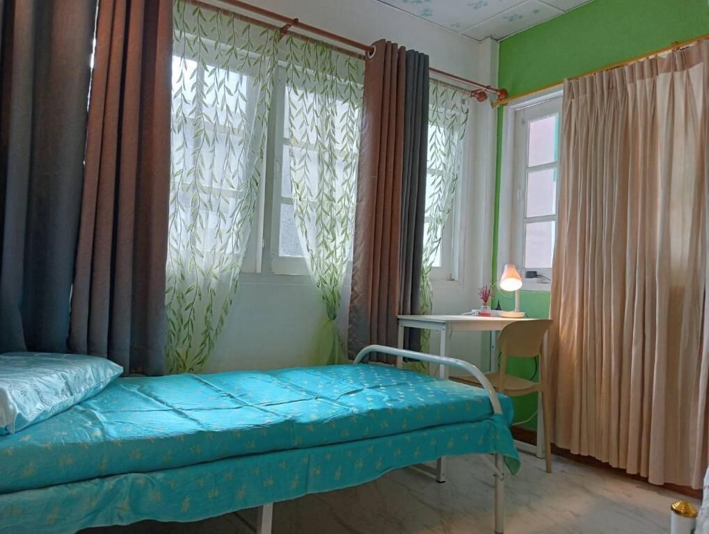 A room with a bed, a desk with a lamp, and a window with curtains.