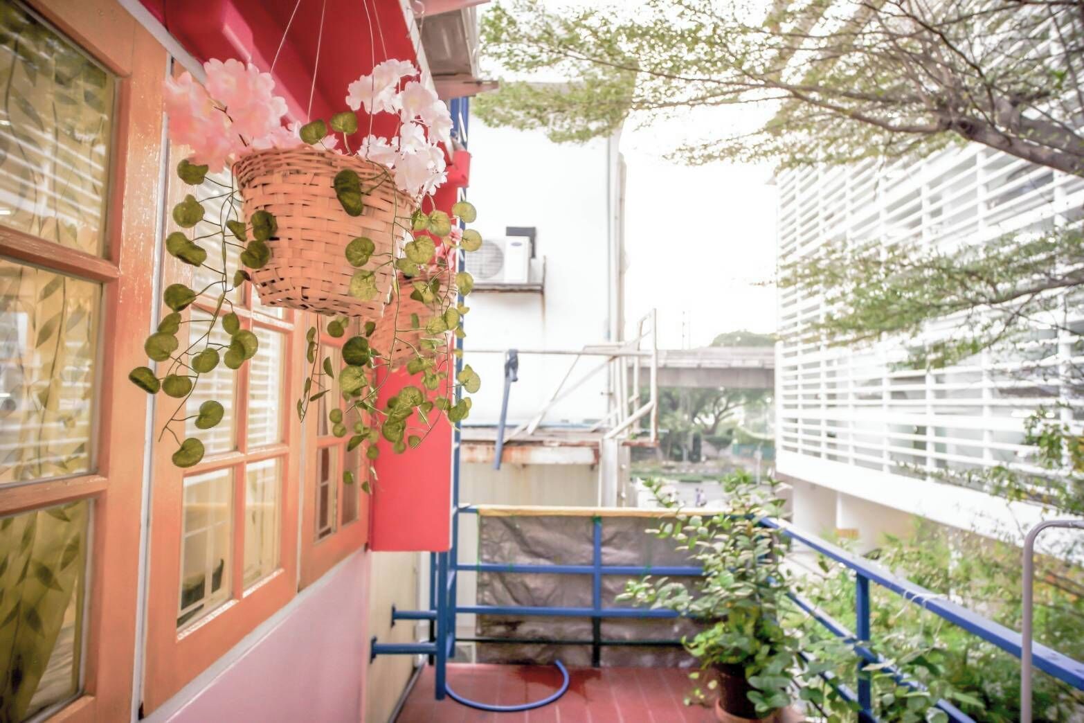 Un balcón con un muro rojo, una cesta de mimbre con plantas colgantes y una barandilla azul.