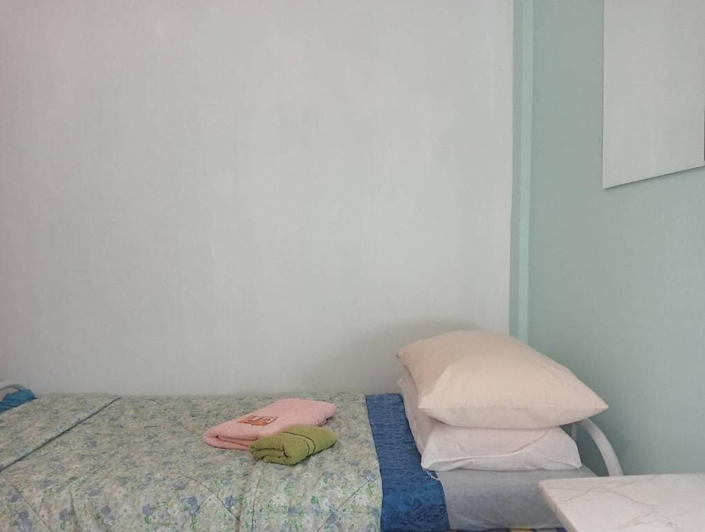 A single bed with a floral-patterned bedspread, a blue blanket, and two pillows.