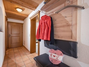 A hallway with a wooden door, a coat rack with a red jacket, and a black bench with a checkered bag. - Zuppinger by Interhome (Mayrhofen)
