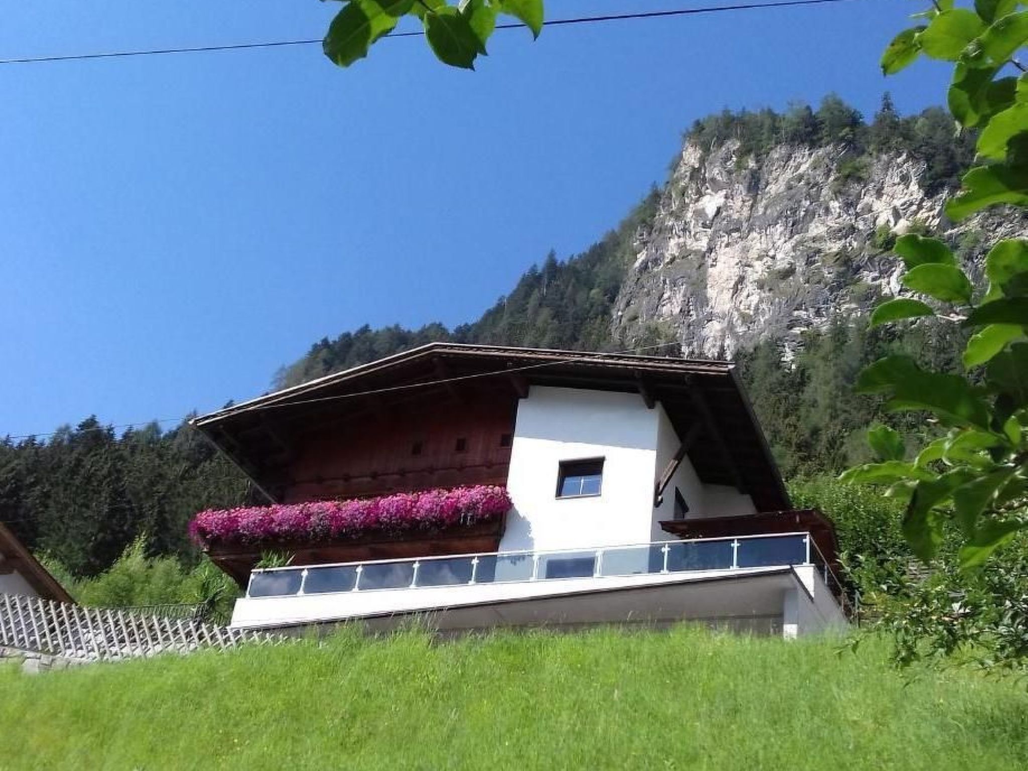 Ein Chalet mit Balkon, umgeben von Grün und einer Bergkulisse.