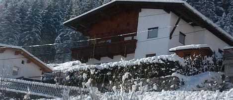 A chalet with a sloped roof, wooden balcony, and snow-covered surroundings.