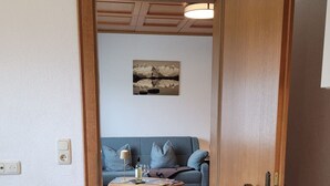 A narrow hallway leading to a living area with a sofa and a coffee table, a wooden floor, and a door with a handle. - Zuppinger by Interhome (Mayrhofen)