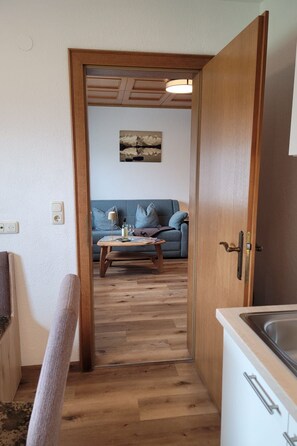 A narrow hallway leading to a living area with a sofa and a coffee table, a wooden floor, and a door with a handle. - Zuppinger by Interhome (Mayrhofen)
