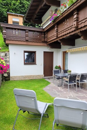 Une terrasse avec une table et des chaises, un balcon en bois orné de fleurs et un chemin pavé de pierres.