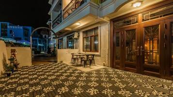 A hotel exterior with a paved patio, outdoor seating, and a well-lit entrance.
