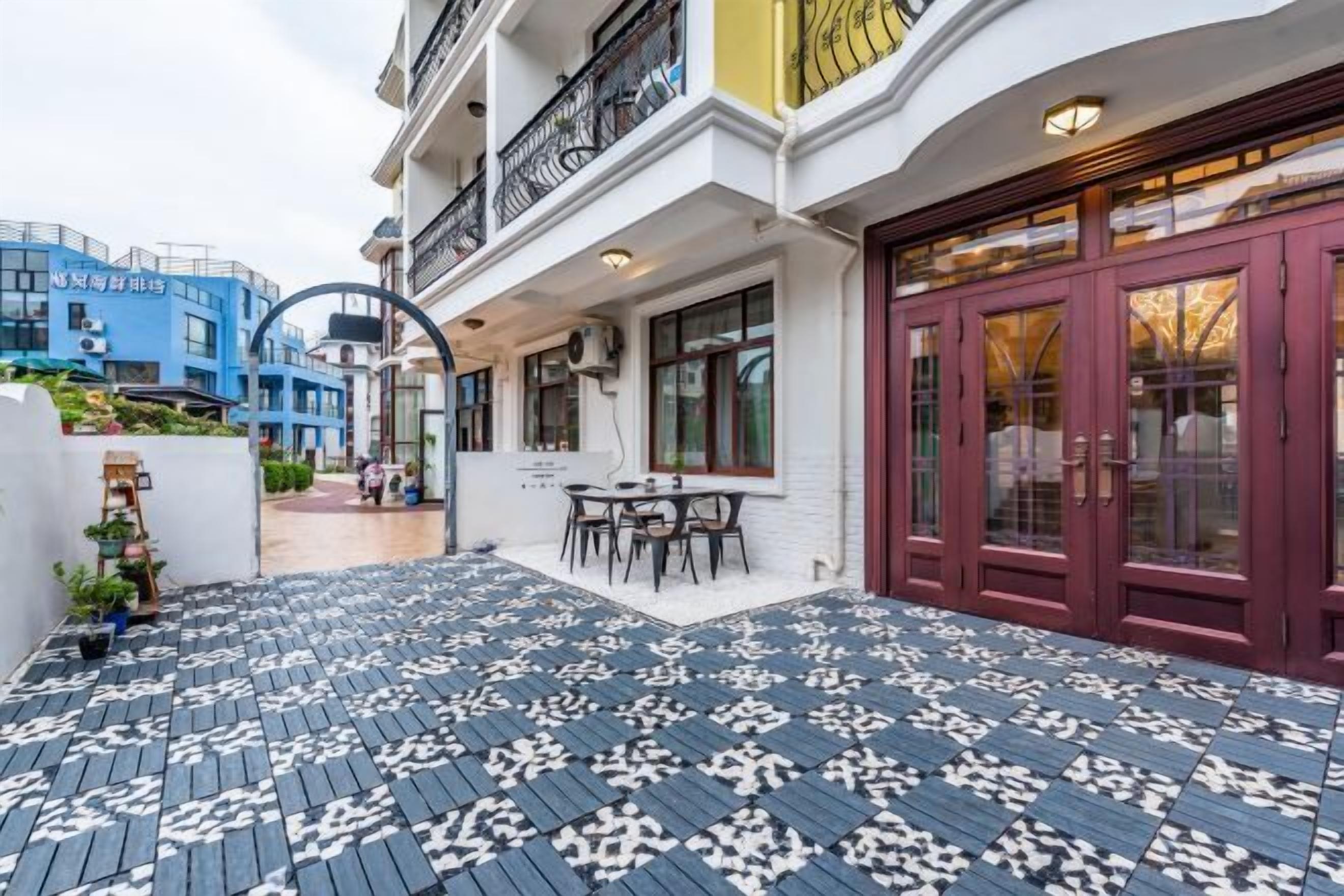 A building with a red door, a balcony with a patterned floor, and a table with chairs outside.