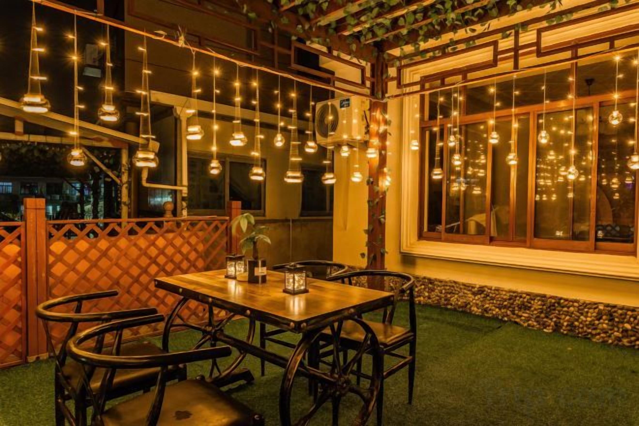 Un espace de restauration en plein air avec une table et des chaises, des guirlandes lumineuses et une vue sur la ville la nuit.