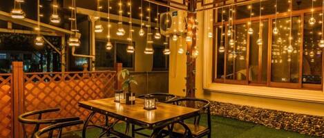 Un espace de restauration en plein air avec une table et des chaises, des guirlandes lumineuses et une vue sur la ville la nuit.