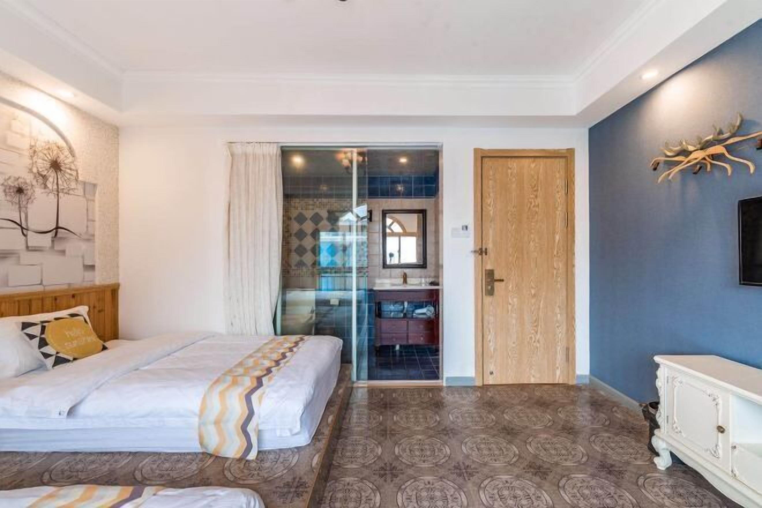 A bedroom with a bed, a dresser, and a glass door leading to a bathroom.